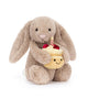 bashful beige birthday bunny, plush beige bunny holding a smiling birthday cake topped with strawberries and a candle