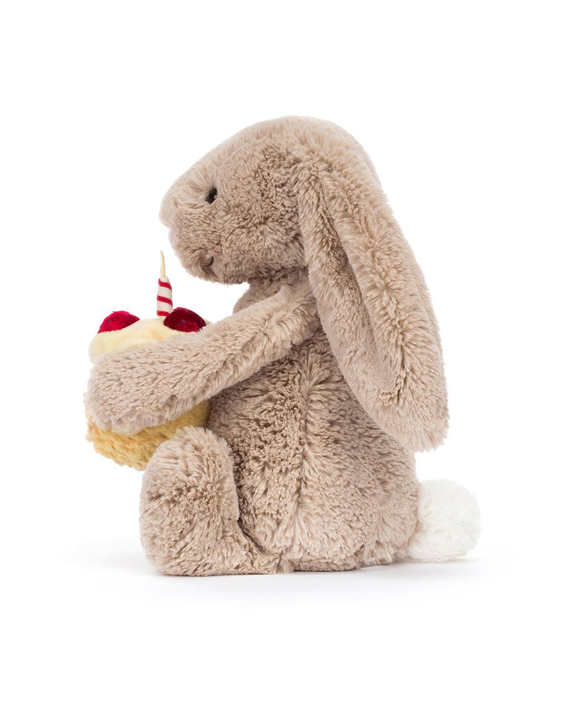bashful beige birthday bunny, plush beige bunny holding a smiling birthday cake topped with strawberries and a candle