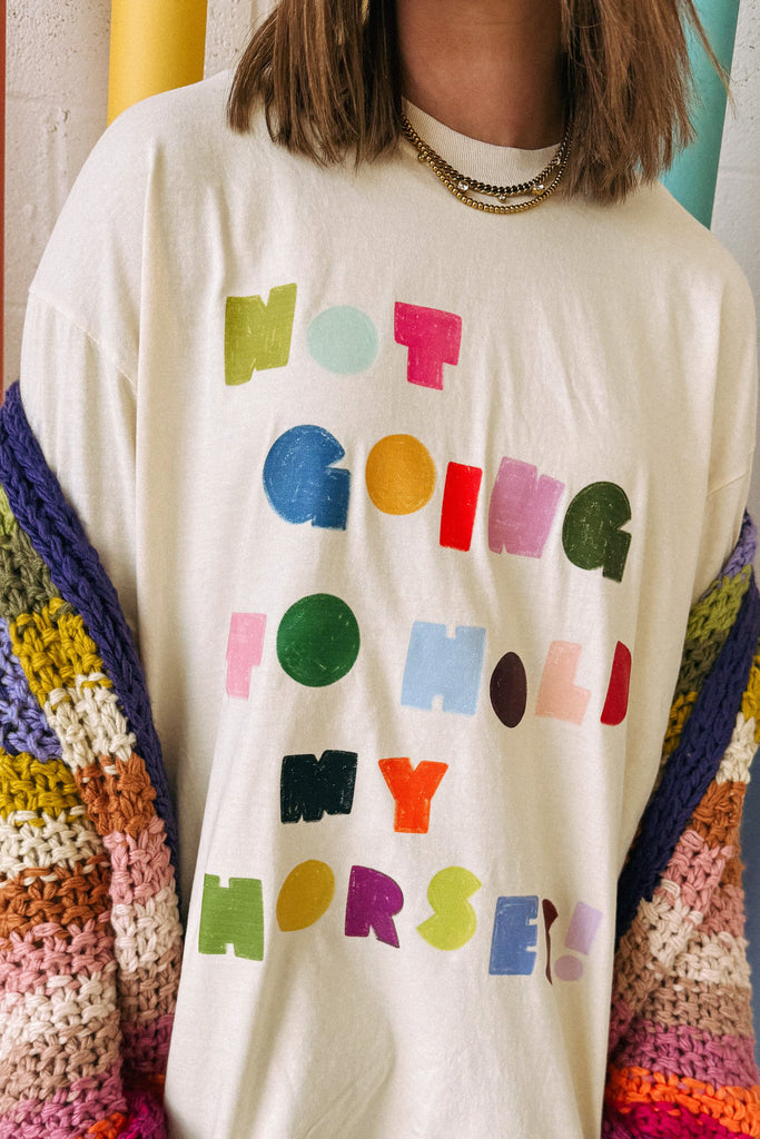 white graphic tee with the message "not going to hold my horses" in a bold and colorful design
