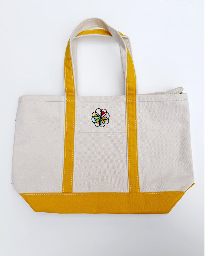canvas tote with mustard yellow trim and colorfully embroidered personify flower logo