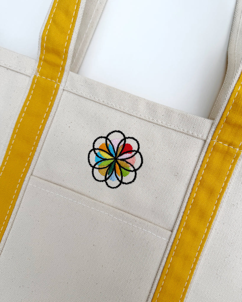 canvas tote with mustard yellow trim and colorfully embroidered personify flower logo