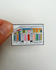 lapel pin featuring an illustration of personify duluth's storefront