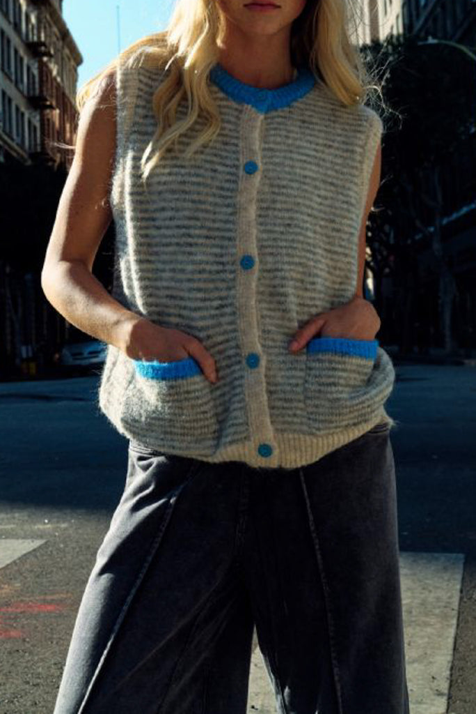 knit sweater vest in cream and light grey with bright blue detailing on buttons, neckline, and pockets