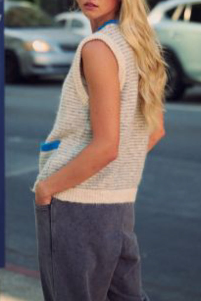 knit sweater vest in cream and light grey with bright blue detailing on buttons, neckline, and pockets